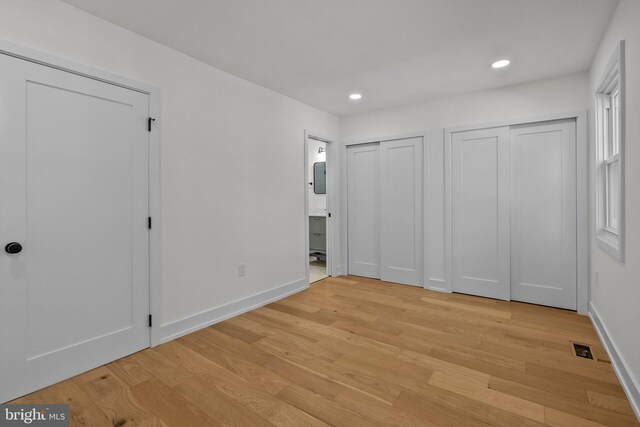 unfurnished bedroom featuring multiple closets, ensuite bathroom, and light hardwood / wood-style flooring