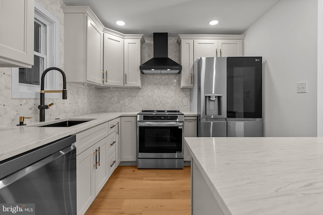 kitchen featuring stainless steel appliances, sink, wall chimney range hood, white cabinets, and light hardwood / wood-style floors