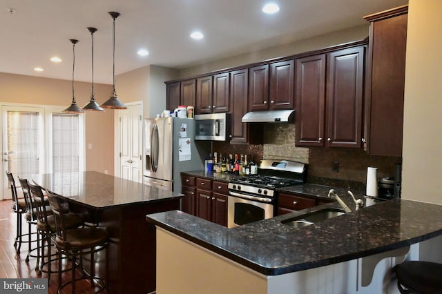 kitchen featuring a kitchen breakfast bar, stainless steel appliances, sink, decorative light fixtures, and light hardwood / wood-style flooring