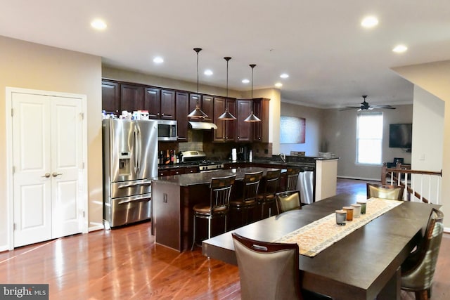 kitchen with ceiling fan, a center island, hanging light fixtures, stainless steel appliances, and a kitchen bar