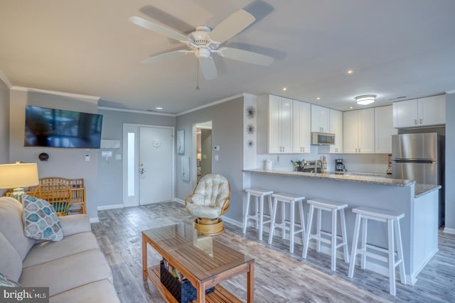 living room featuring ceiling fan, sink, ornamental molding, and light wood-type flooring