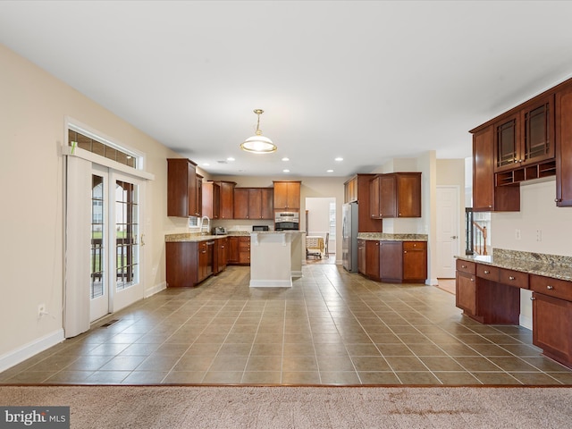 kitchen featuring light stone counters, decorative light fixtures, a kitchen island, dark tile patterned flooring, and appliances with stainless steel finishes