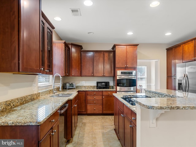 kitchen featuring light stone countertops, stainless steel appliances, sink, light tile patterned floors, and a center island