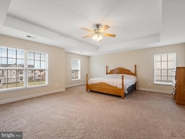 carpeted bedroom with a raised ceiling and ceiling fan