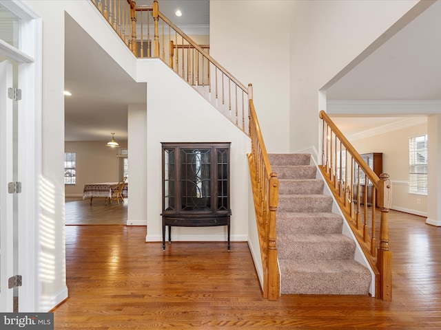 stairway with a high ceiling, hardwood / wood-style flooring, and ornamental molding