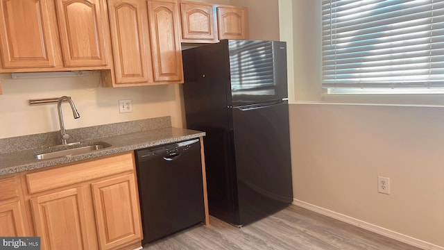 kitchen featuring black appliances, light hardwood / wood-style floors, sink, and dark stone counters