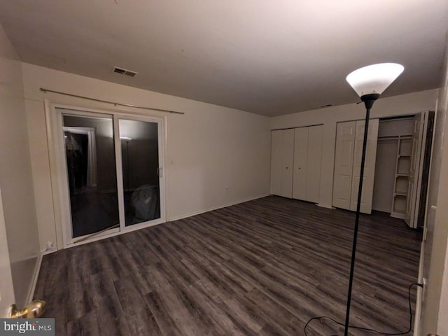 unfurnished bedroom featuring two closets and dark hardwood / wood-style floors