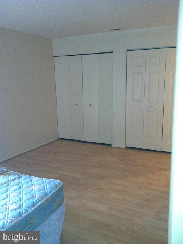 unfurnished bedroom featuring light hardwood / wood-style flooring and multiple closets