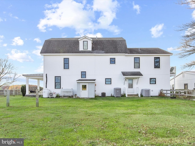 rear view of property with central air condition unit and a lawn