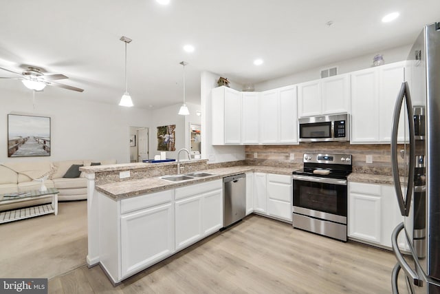 kitchen with kitchen peninsula, appliances with stainless steel finishes, sink, decorative light fixtures, and light hardwood / wood-style floors