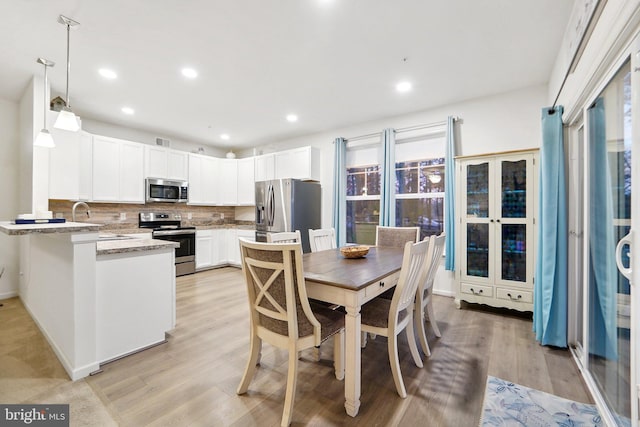 kitchen with appliances with stainless steel finishes, backsplash, light stone counters, decorative light fixtures, and light hardwood / wood-style floors