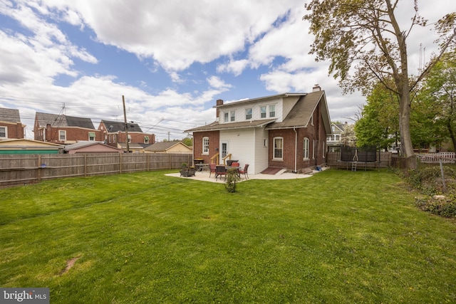 back of property with a yard, a patio, and a trampoline