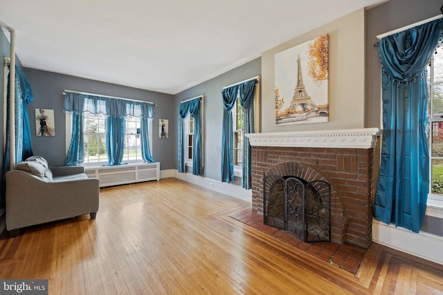 living room featuring hardwood / wood-style flooring, radiator heating unit, and a brick fireplace