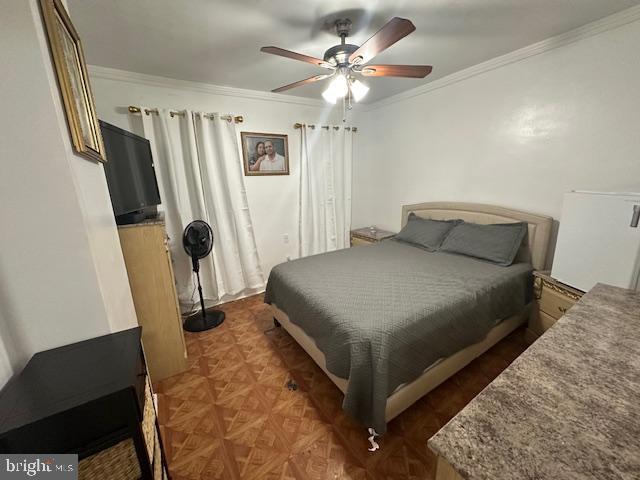 bedroom with dark parquet flooring, ceiling fan, and crown molding