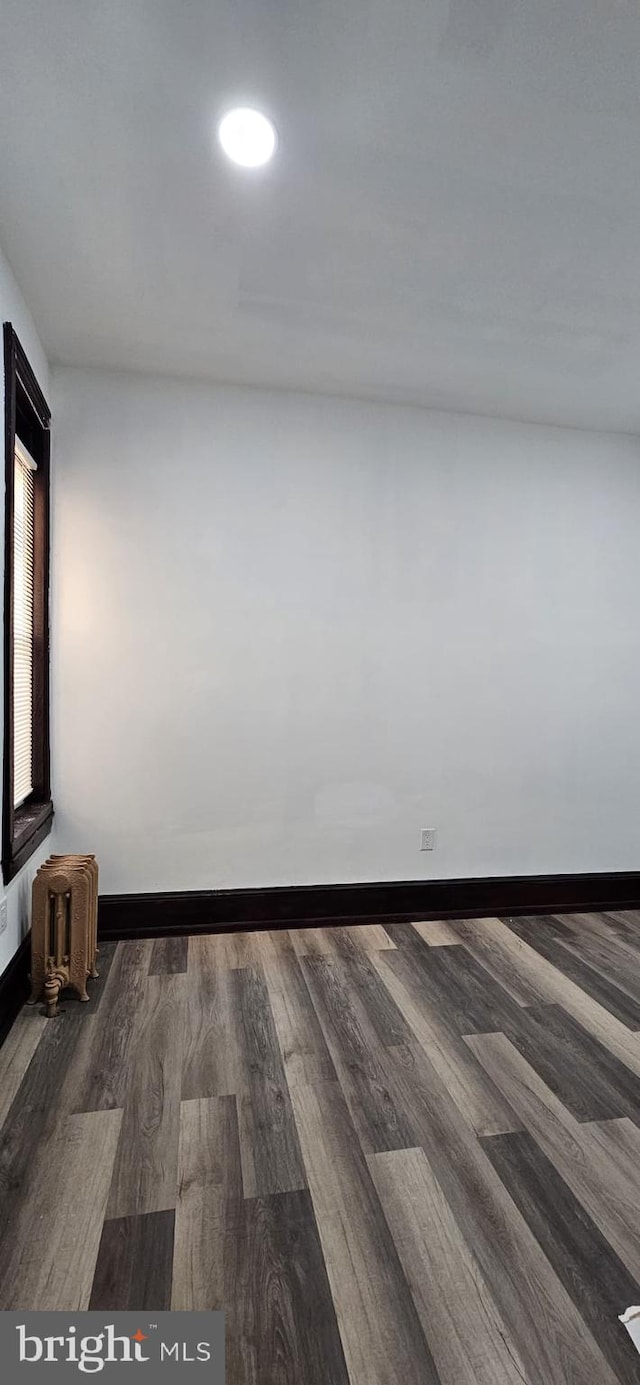 empty room with dark hardwood / wood-style flooring and radiator heating unit