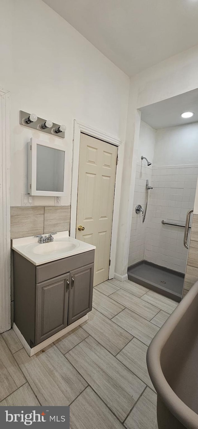 bathroom with vanity, backsplash, and tiled shower