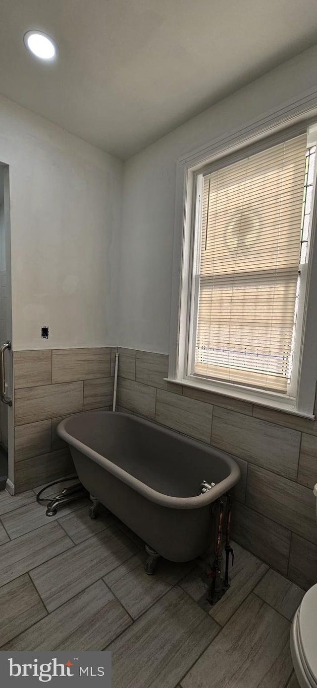 bathroom with toilet, tile walls, and a washtub