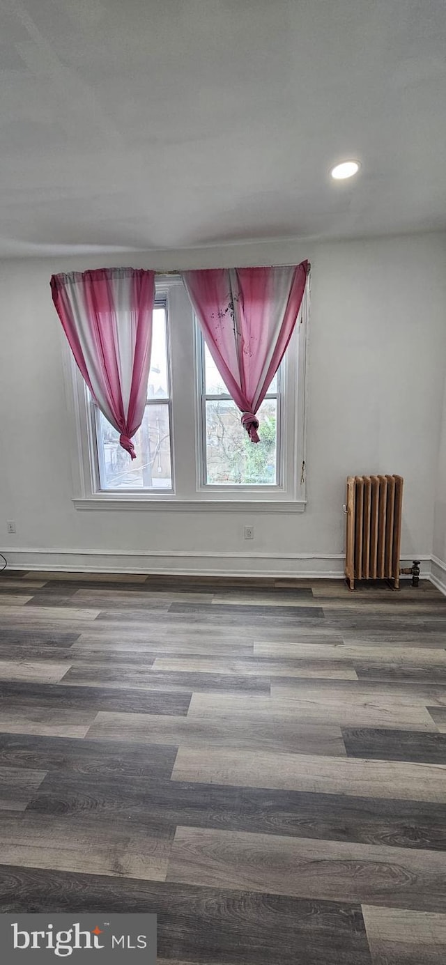 spare room featuring radiator, dark hardwood / wood-style flooring, and a healthy amount of sunlight