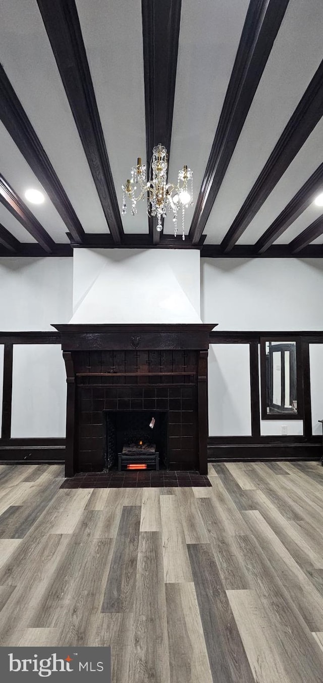 interior space featuring wood-type flooring, ornamental molding, beam ceiling, and a fireplace