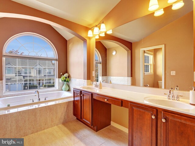 bathroom featuring vanity, tile patterned floors, vaulted ceiling, toilet, and tiled bath