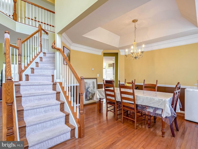 dining room featuring a chandelier, wood-type flooring, a tray ceiling, and ornamental molding