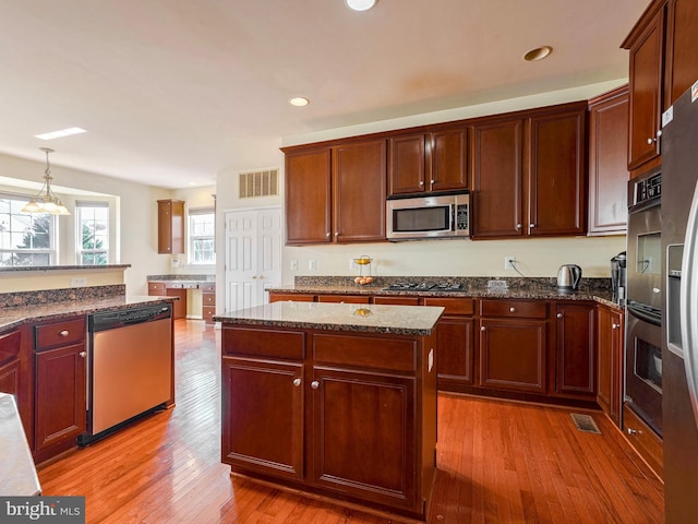 kitchen with dark stone counters, a kitchen island, appliances with stainless steel finishes, decorative light fixtures, and light hardwood / wood-style floors