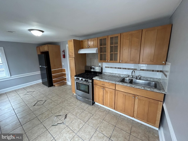 kitchen featuring stainless steel gas stove, sink, tasteful backsplash, black fridge, and light tile patterned flooring