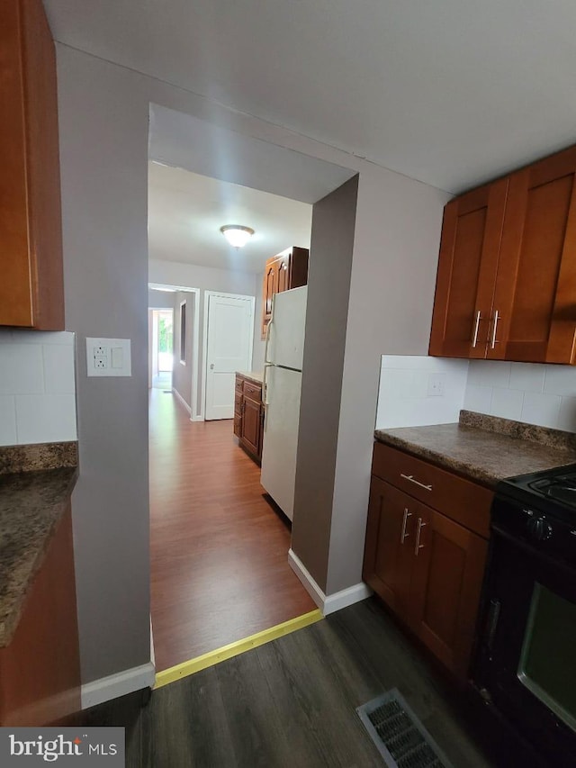 kitchen featuring dark hardwood / wood-style flooring, white refrigerator, tasteful backsplash, and black range oven