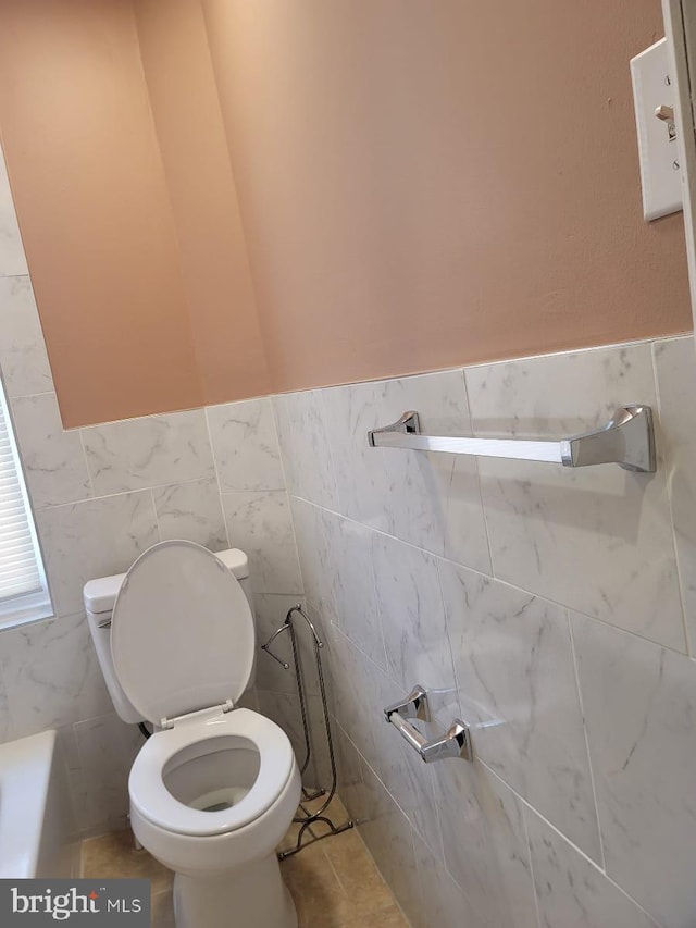 bathroom featuring tile patterned floors, a tub to relax in, toilet, and tile walls