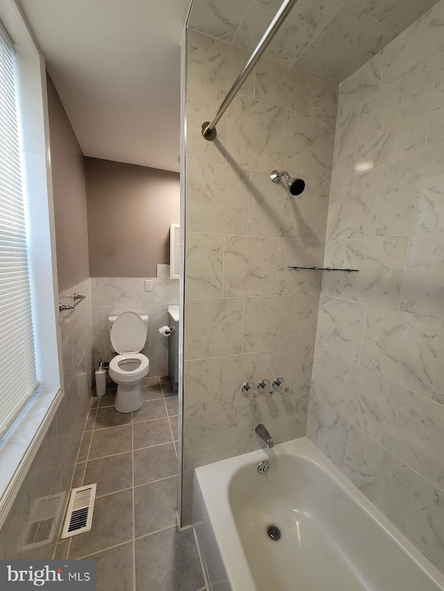 bathroom with tile patterned flooring, tiled shower / bath combo, toilet, and tile walls