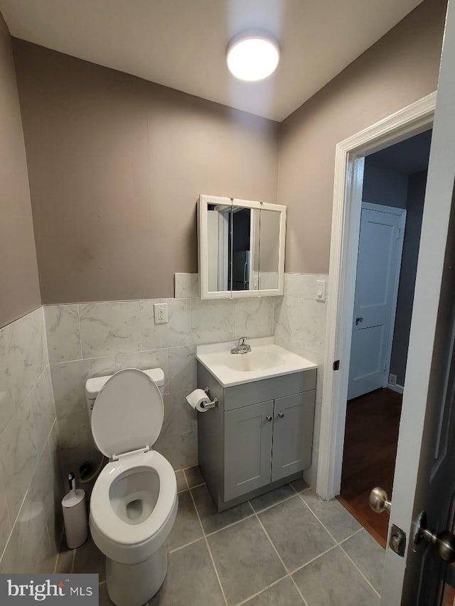 bathroom with toilet, vanity, tile patterned floors, and tile walls