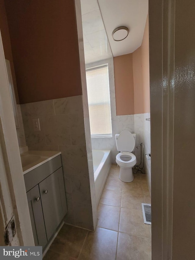 bathroom with tile patterned floors, a bathing tub, toilet, and tile walls