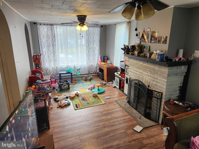 recreation room featuring hardwood / wood-style flooring, a brick fireplace, and ceiling fan