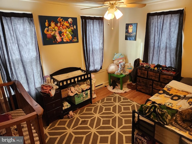 bedroom featuring ceiling fan, wood-type flooring, and a baseboard heating unit