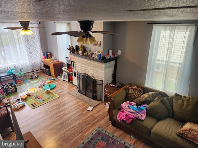 living room with ceiling fan, a fireplace, wood-type flooring, and a textured ceiling