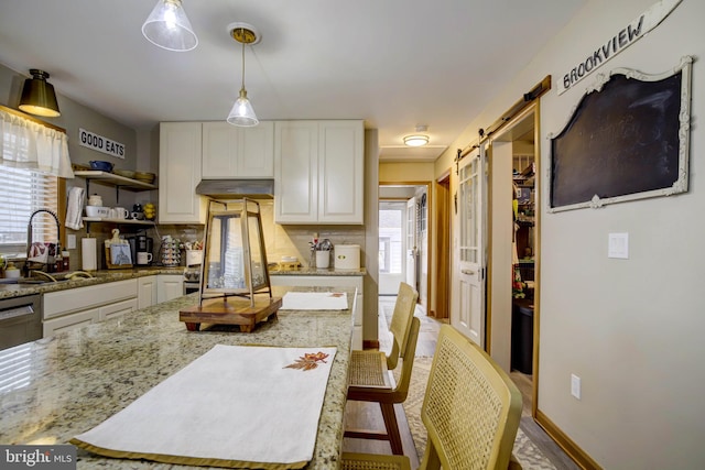 kitchen with backsplash, sink, a barn door, white cabinets, and a center island
