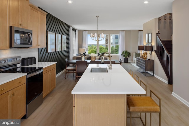 kitchen featuring a center island with sink, sink, light hardwood / wood-style flooring, appliances with stainless steel finishes, and decorative light fixtures