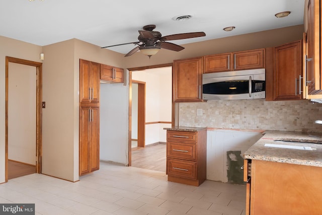 kitchen featuring tasteful backsplash, light stone counters, ceiling fan, and sink