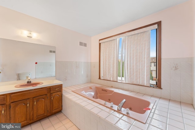 bathroom with tile patterned flooring, vanity, toilet, and tiled bath