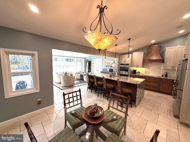 kitchen with a breakfast bar, stainless steel appliances, backsplash, vaulted ceiling, and premium range hood