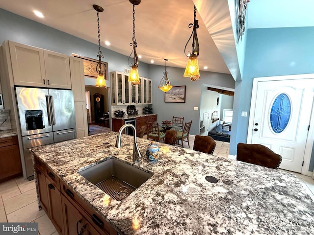 kitchen featuring pendant lighting, high end fridge, glass insert cabinets, stone countertops, and a sink