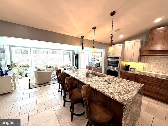 kitchen with light stone counters, stainless steel double oven, premium range hood, backsplash, and stovetop