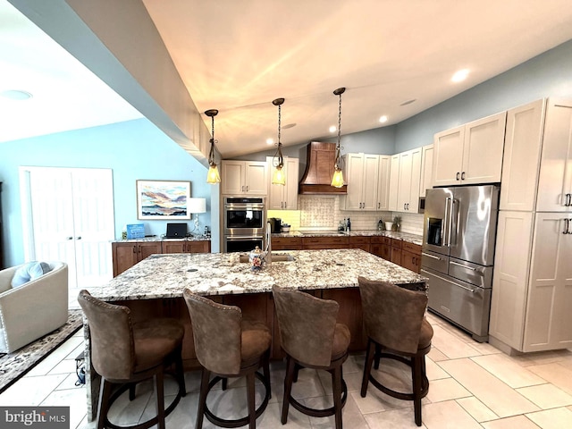 kitchen with lofted ceiling, stainless steel appliances, premium range hood, decorative backsplash, and light stone countertops