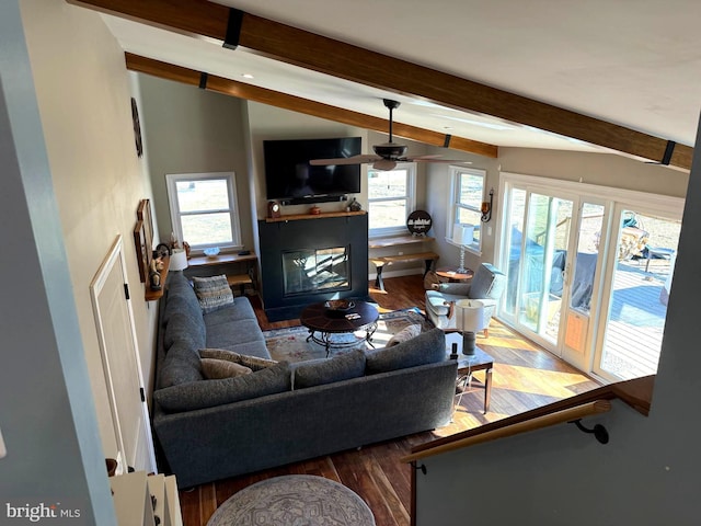 living room with a glass covered fireplace, a healthy amount of sunlight, vaulted ceiling with beams, and wood finished floors