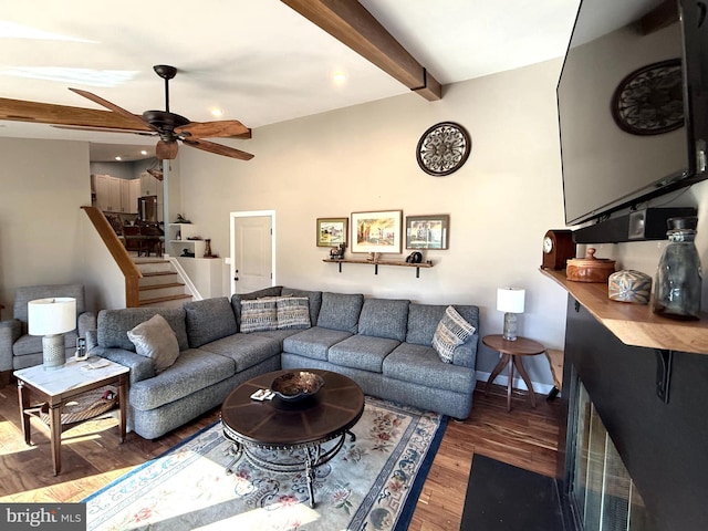 living area with beam ceiling, ceiling fan, wood finished floors, baseboards, and stairs