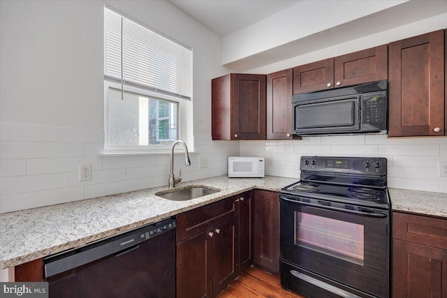 kitchen featuring light wood-type flooring, sink, light stone counters, and black appliances