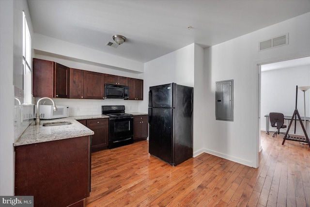 kitchen with light stone counters, light hardwood / wood-style floors, sink, black appliances, and electric panel