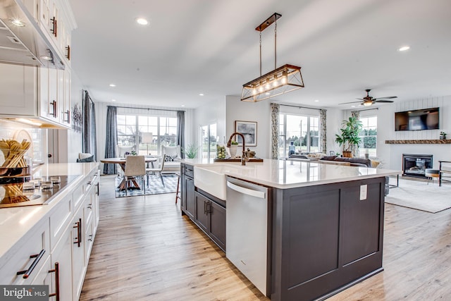 kitchen with dishwasher, white cabinets, a center island with sink, hanging light fixtures, and light hardwood / wood-style flooring