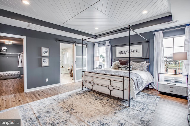 bedroom with a barn door, light hardwood / wood-style flooring, wooden ceiling, and connected bathroom