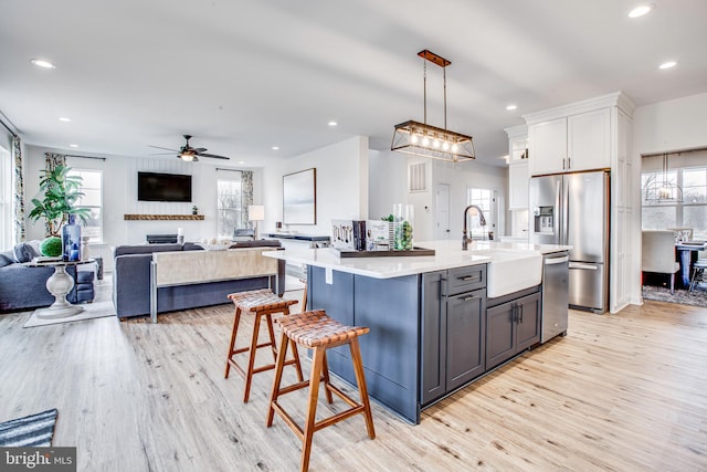 kitchen with white cabinets, decorative light fixtures, light wood-type flooring, and stainless steel appliances